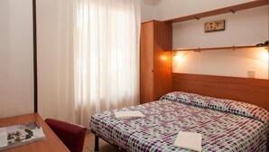 Une chambre d’hôtel avec un lit, une tête de lit en bois, une table avec un magazine et une fenêtre avec des rideaux.