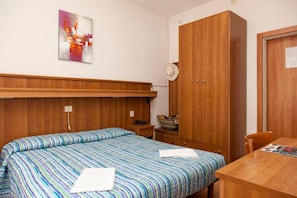 Una camera da letto con un letto di legno, un armadio in legno, un comodino con una lampada e un tavolino con una rivista.