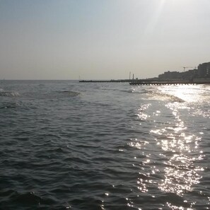 A calm sea with a pier extending into the water, buildings in the background, and a clear sky. - Hotel Taormina (Jesolo)