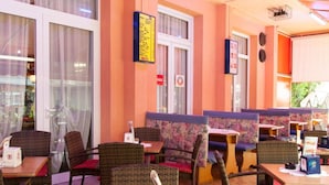 Un espace de détente intérieur avec des meubles en osier, un panneau affichant le menu et une fenêtre agrémentée de rideaux.