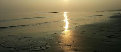 A beach with a sun reflecting on the wet sand, creating a path of light.