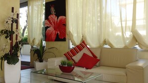 Un salon avec un canapé, une table basse en verre et un grand tableau représentant une fleur rouge.