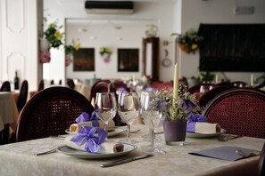 A dining table set with plates, wine glasses, and a candle, surrounded by chairs. - Hotel Beny (Jesolo)