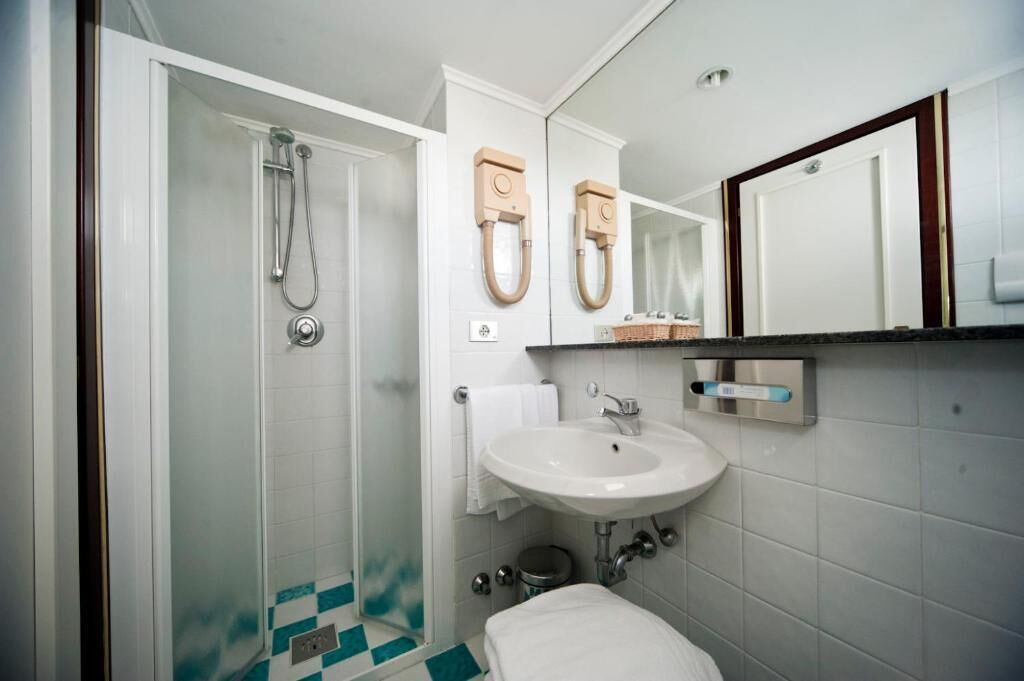 A bathroom with a glass shower enclosure, a white sink, a mirror, and a towel rack.