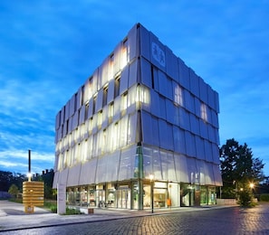 A modern building with a glass facade, multiple floors, and a visible entrance with glass doors. - Hotel Rossi (Berlin)