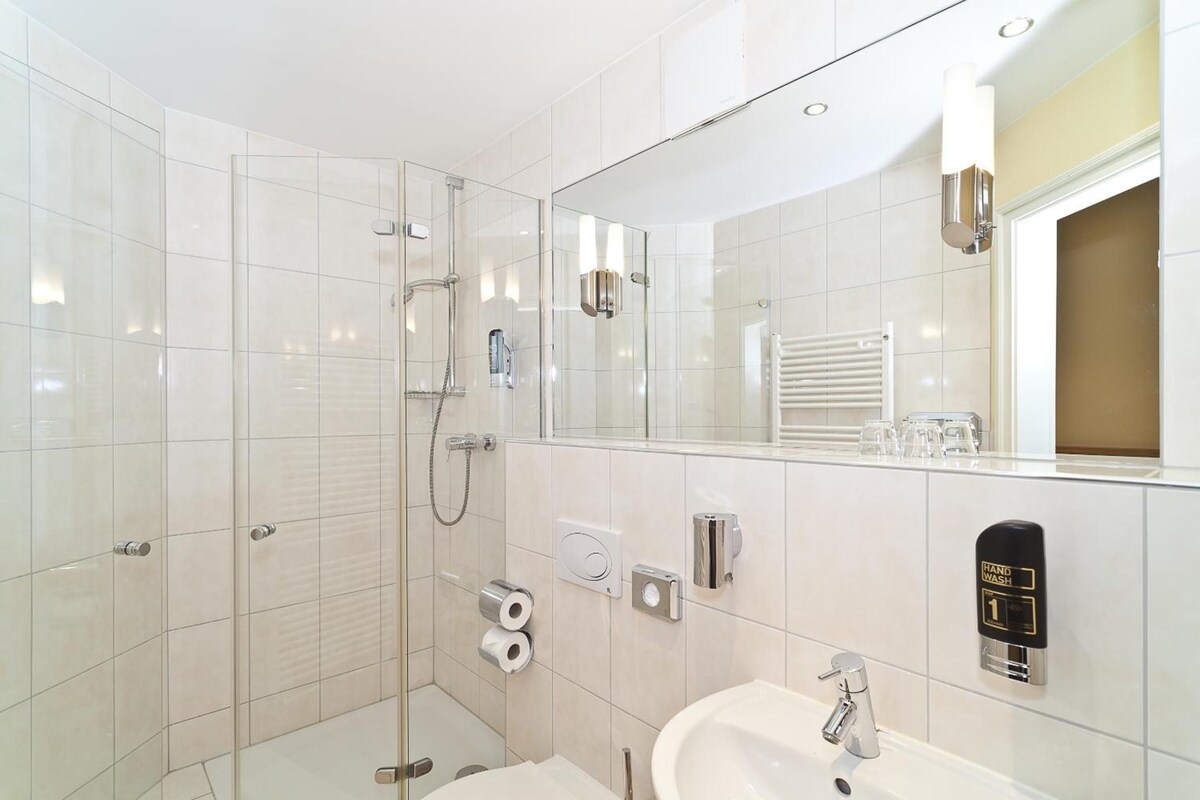Een moderne badkamer met een douchecabine van glas, een wastafel en een spiegel.