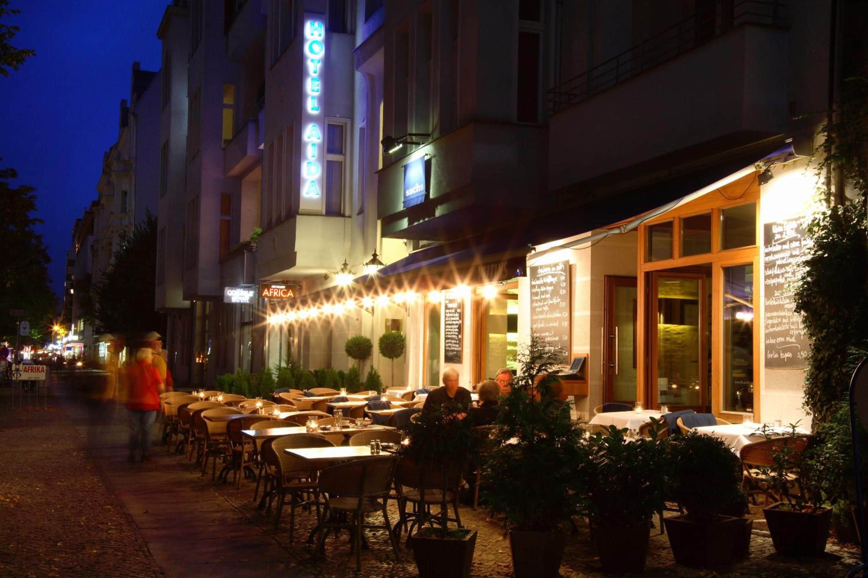 A hotel with outdoor seating, a neon sign, and a menu board.
