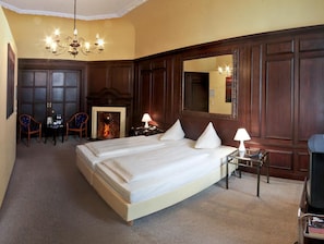 A hotel room with a large bed, a fireplace, a mirror, and a chandelier.