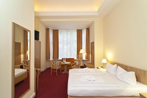 Een hotelkamer met een groot bed, een bureau met twee stoelen, een televisie en een raam met gordijnen.