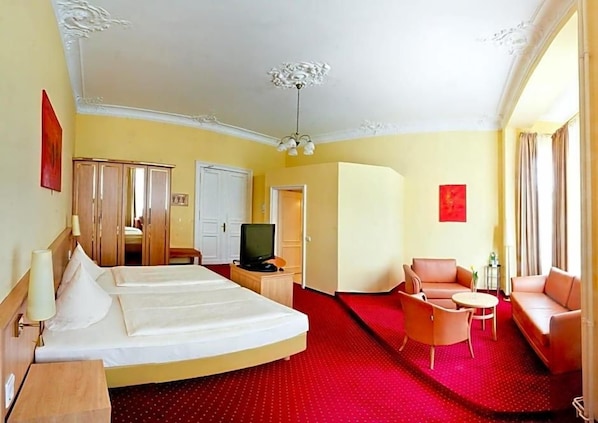 A hotel room with two beds, a television, a sofa, and a red carpet.