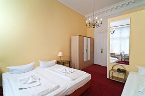 Une chambre d’hôtel avec un lit, une armoire, un miroir, un lustre et une moquette rouge.