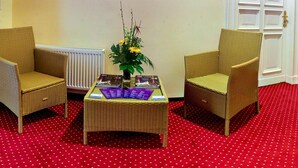 Une pièce comprenant deux fauteuils en osier, une table basse ornée d’un vase de fleurs et un radiateur.