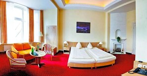 Een hotelkamer met een bed, een bank, een stoel, een tafeltje, een open haard en een schilderij aan de muur.