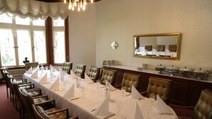 Une salle à manger élégante, avec de longues tables dressées pour le repas, des fauteuils en cuir et un grand miroir au mur.