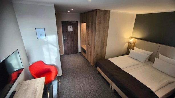 Une chambre d’hôtel comprenant un lit, un bureau avec une chaise, une armoire et une porte donnant sur une autre pièce.
