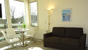 Un salon avec un canapé marron, des fauteuils blancs, une petite table ronde et un lampadaire.