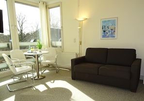A living room with a brown sofa, white chairs, a small round table, and a floor lamp. - St.-michaels-heim Jugendgastehaus & Hotel (Berlin)