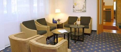 A hotel room with a seating area featuring two sofas and two armchairs, a small round table, and a lamp.