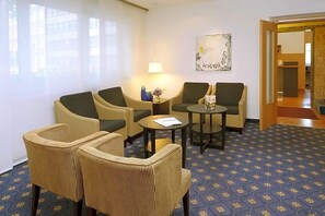 A hotel room with a seating area featuring two sofas and two armchairs, a small round table, and a lamp. - Hotel Ludwig Superior (Cologne)
