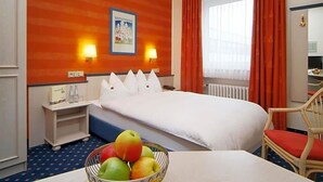 A hotel room with a bed, bedside tables, a fruit bowl, a window with curtains, and a painting on the wall. - Hotel Ludwig Superior (Cologne)