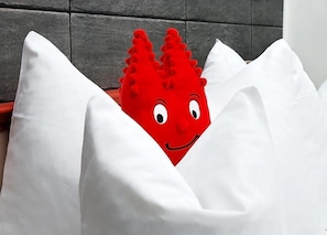 A red object with a face peeking out from behind white pillows. - Hotel Ludwig Superior (Cologne)