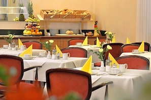 A dining area with multiple tables set for breakfast, each with a white tablecloth, yellow napkins, and a variety of breakfast items. - Hotel Ludwig Superior (Cologne)