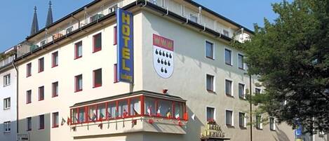 Un hôtel reconnaissable à son enseigne bien visible, à ses nombreuses fenêtres et à son balcon orné de drapeaux.