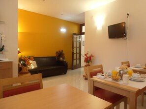 A dining area with a table set for breakfast, a sofa, and a TV mounted on the wall. - Hotel S Marino (Porto)