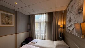 A hotel room with two beds, a large window with curtains, a painting on the wall, and a lamp. - Hotel Mevlana (Amsterdam)