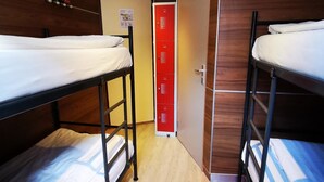 A dormitory room with bunk beds, a wooden floor, a red storage unit, and a door with a poster. - Hotel Mevlana (Amsterdam)