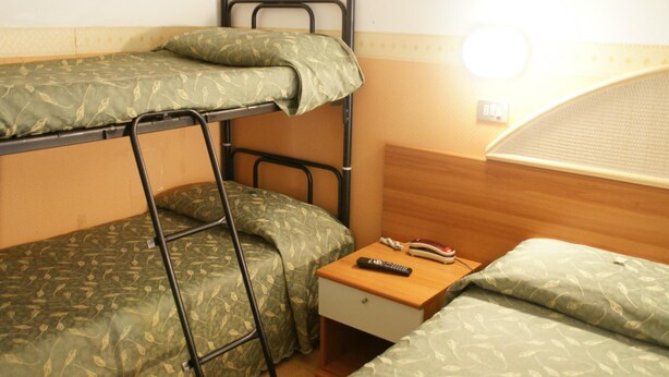 Une chambre avec un lit superposé, une échelle, une table de chevet avec une télécommande et une fenêtre avec des stores.