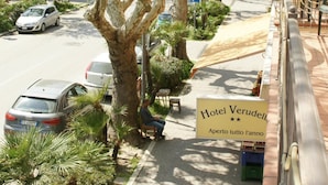 Une rue bordée d’arbres, avec des voitures garées, un banc et un panneau indiquant l’hôtel Verudella.
