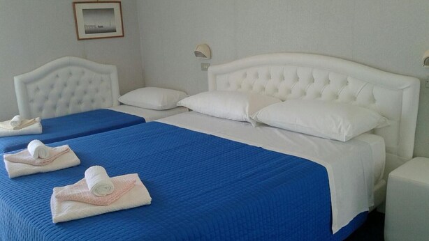 A hotel room with two beds, each with a blue bedspread and white headboards. There are towels neatly folded on the beds. - Hotel Biagini (Rimini)