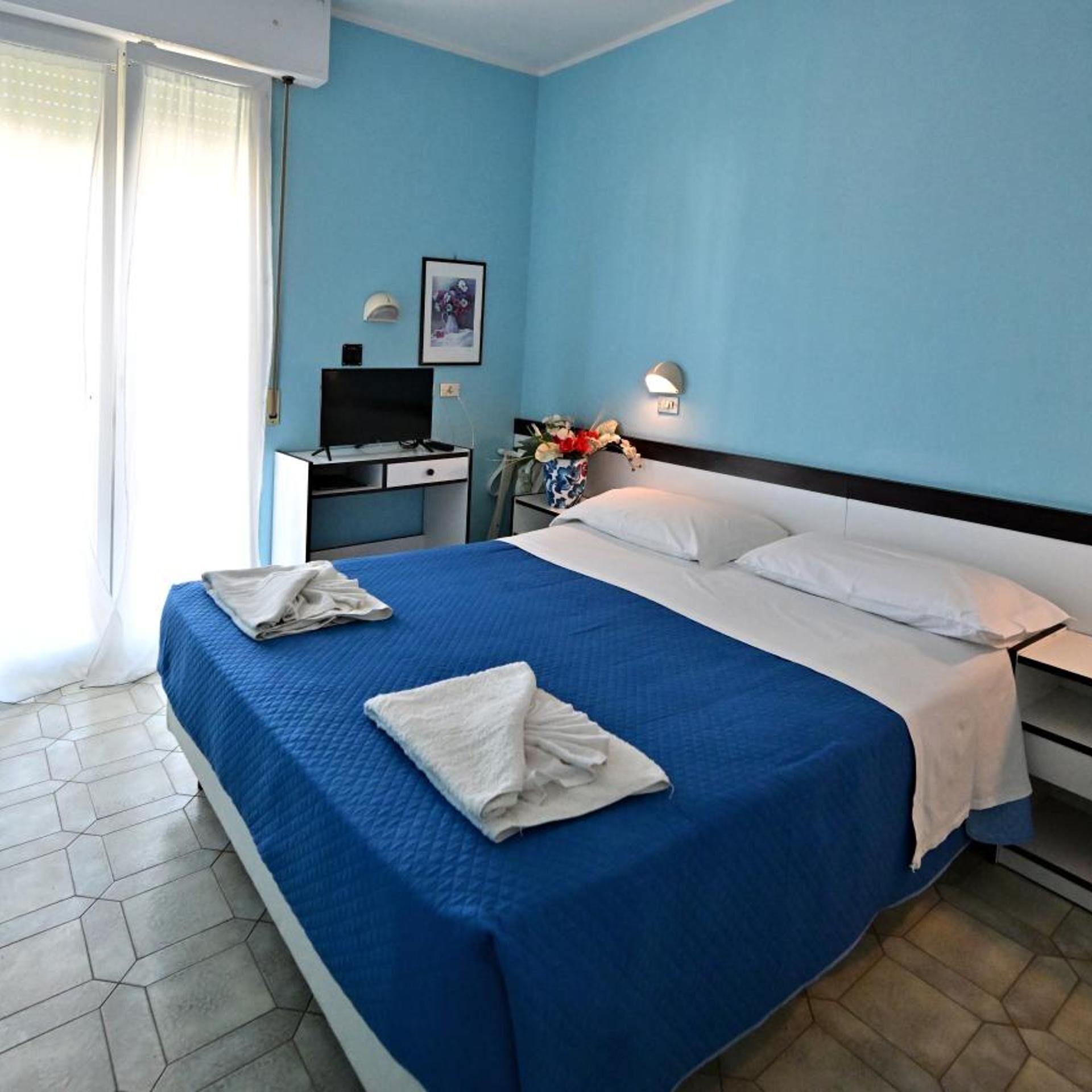 Une chambre d’hôtel avec un grand lit, un bureau, une chaise, une télévision et une fenêtre avec des rideaux.