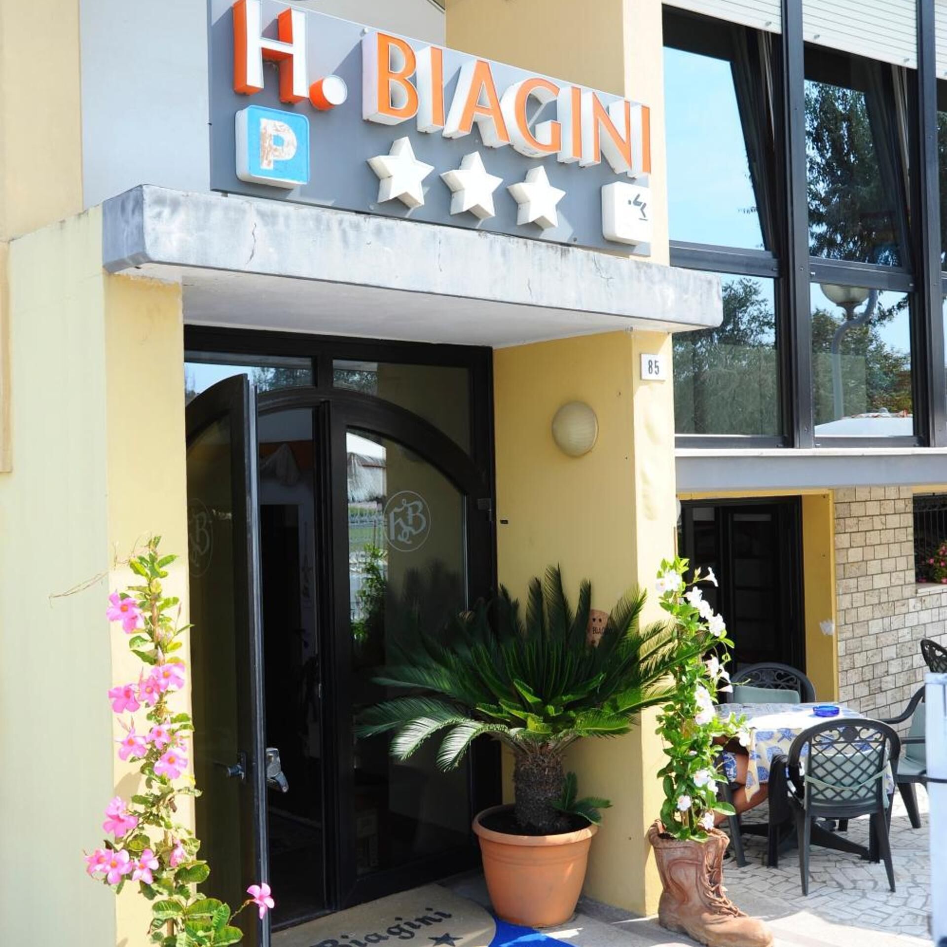 A building with a sign reading 'H. Biagini' and a parking symbol. There are potted plants and a table with chairs outside.