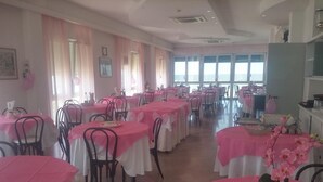 A dining area with round tables covered in pink tablecloths and black chairs. - Hotel Biagini (Rimini)