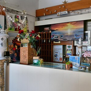 A reception desk with a 'WELCOME' sign, a painting of boats on water, and a 'FREE WiFi' sign. - Hotel Biagini (Rimini)
