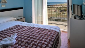 A hotel room with a bed, a desk with a computer, a chair, a window with a view of the beach, and a balcony. - Hotel Biagini (Rimini)