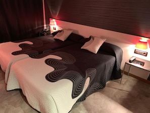 A double bed with a unique wave-patterned bedspread, two bedside lamps, and a nightstand with a phone and remote control. - La Suite Hotel (Vigo)