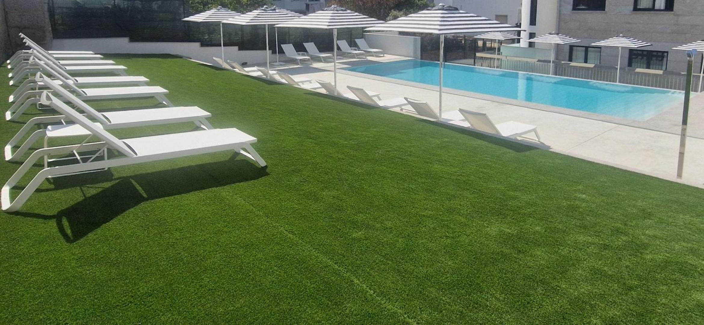 Zona junto a la piscina con sillas de descanso blancas y sombrillas, una piscina y un césped bien cuidado.