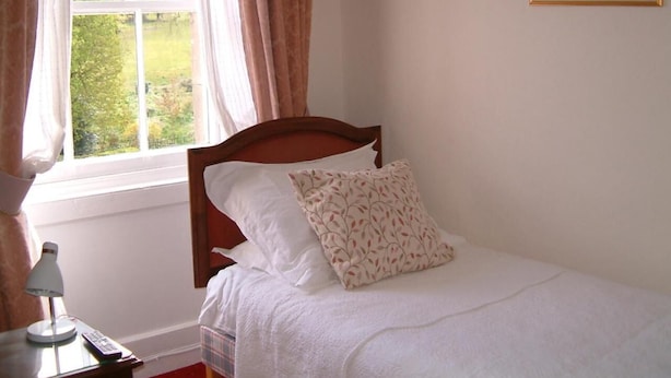 A bedroom with a bed, a nightstand, a lamp, and a window with curtains. - Terrace Hotel (Edinburgh)
