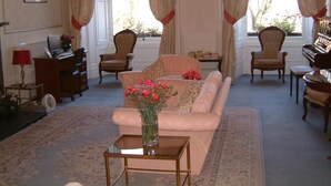 A living room with a sofa, chairs, a small table with a vase of flowers, a piano, and a radiator. - Terrace Hotel (Edinburgh)