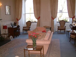 A living room with a sofa, chairs, a small table with a vase of flowers, a piano, and a radiator. - Terrace Hotel (Edinburgh)