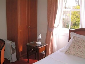 A bedroom with a bed, a nightstand with a lamp, a radiator, and a window with curtains. - Terrace Hotel (Edinburgh)