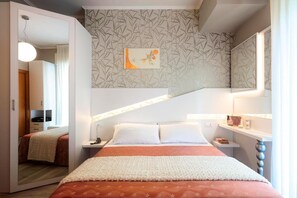 A modern bedroom with a bed, bedside tables, a mirror, and a wall with a leaf-patterned wallpaper. - Hotel Ombretta Mare (Rimini)
