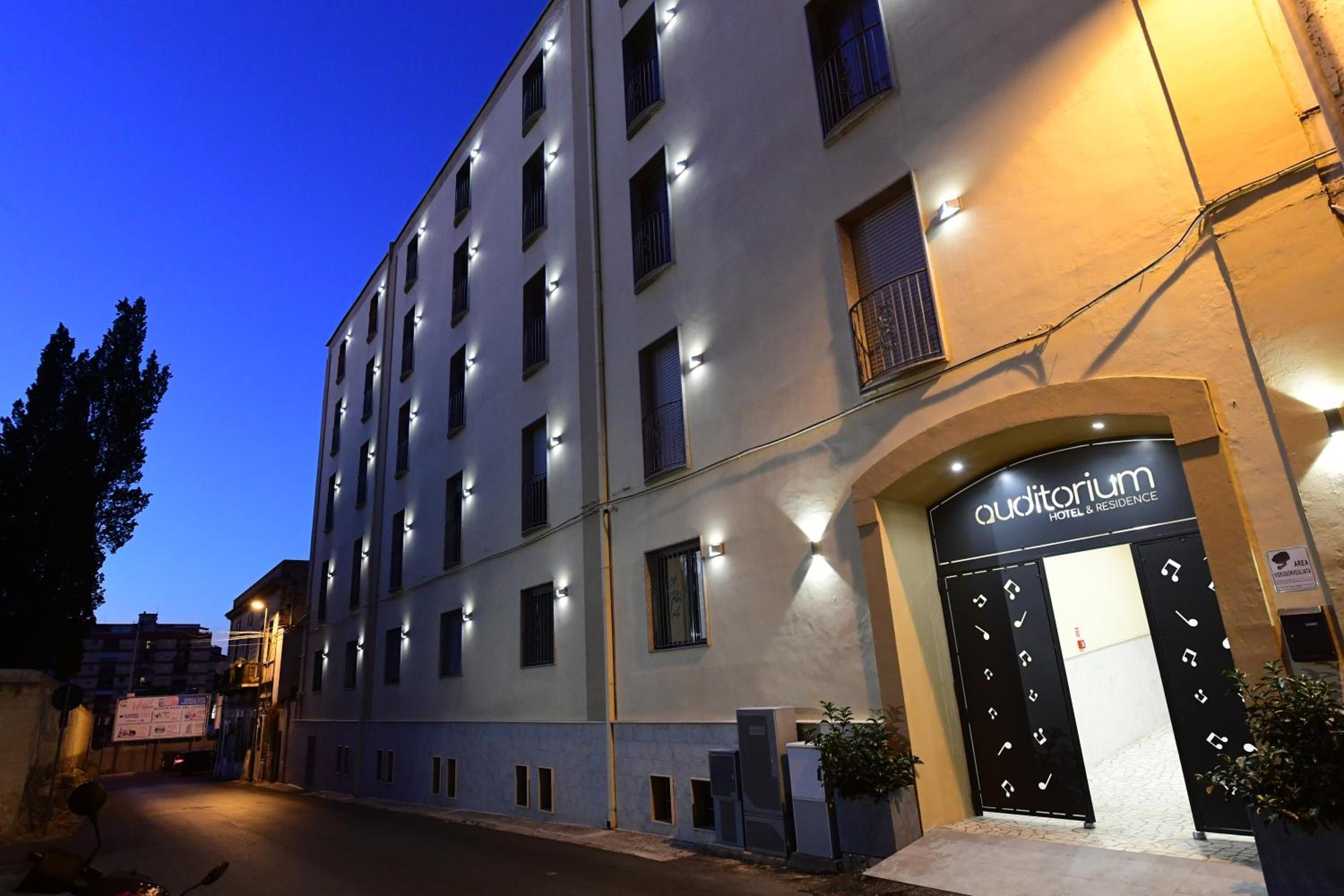 Un hotel a più piani con facciata moderna, caratterizzato da un ingresso in evidenza con una porta nera e un cartello sopra.