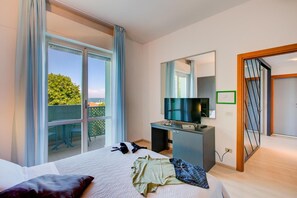 Habitació d'hotel amb un llit, una taula de nit amb televisió, un mirall i un balcó amb vista a vegetació.