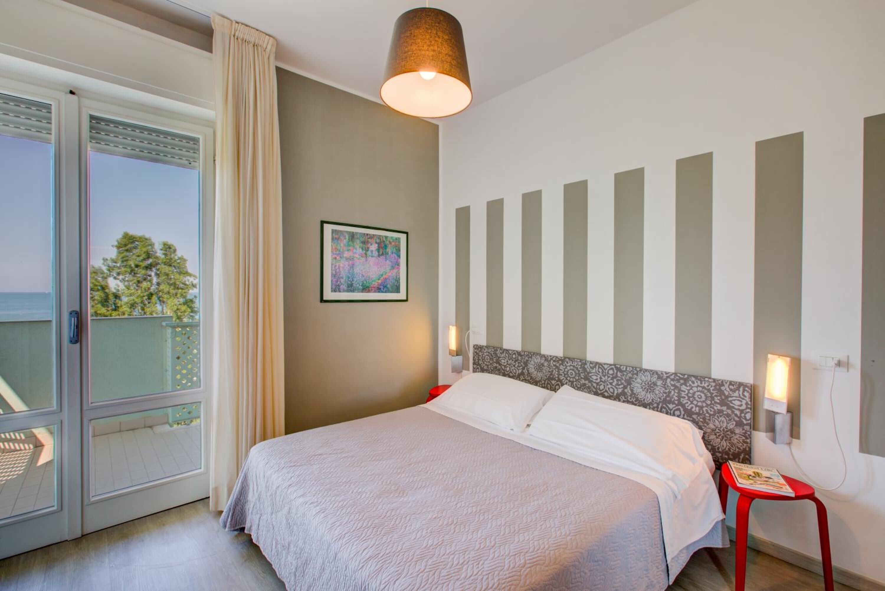 A bedroom with a bed, a window with curtains, a wall-mounted lamp, and a framed picture.