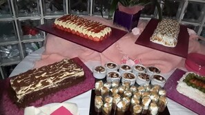 Una mesa de postres con diversos pasteles y dulces, incluyendo un pastel de capas con fresas, un pastel de chocolate y pequeños vasos de postre.