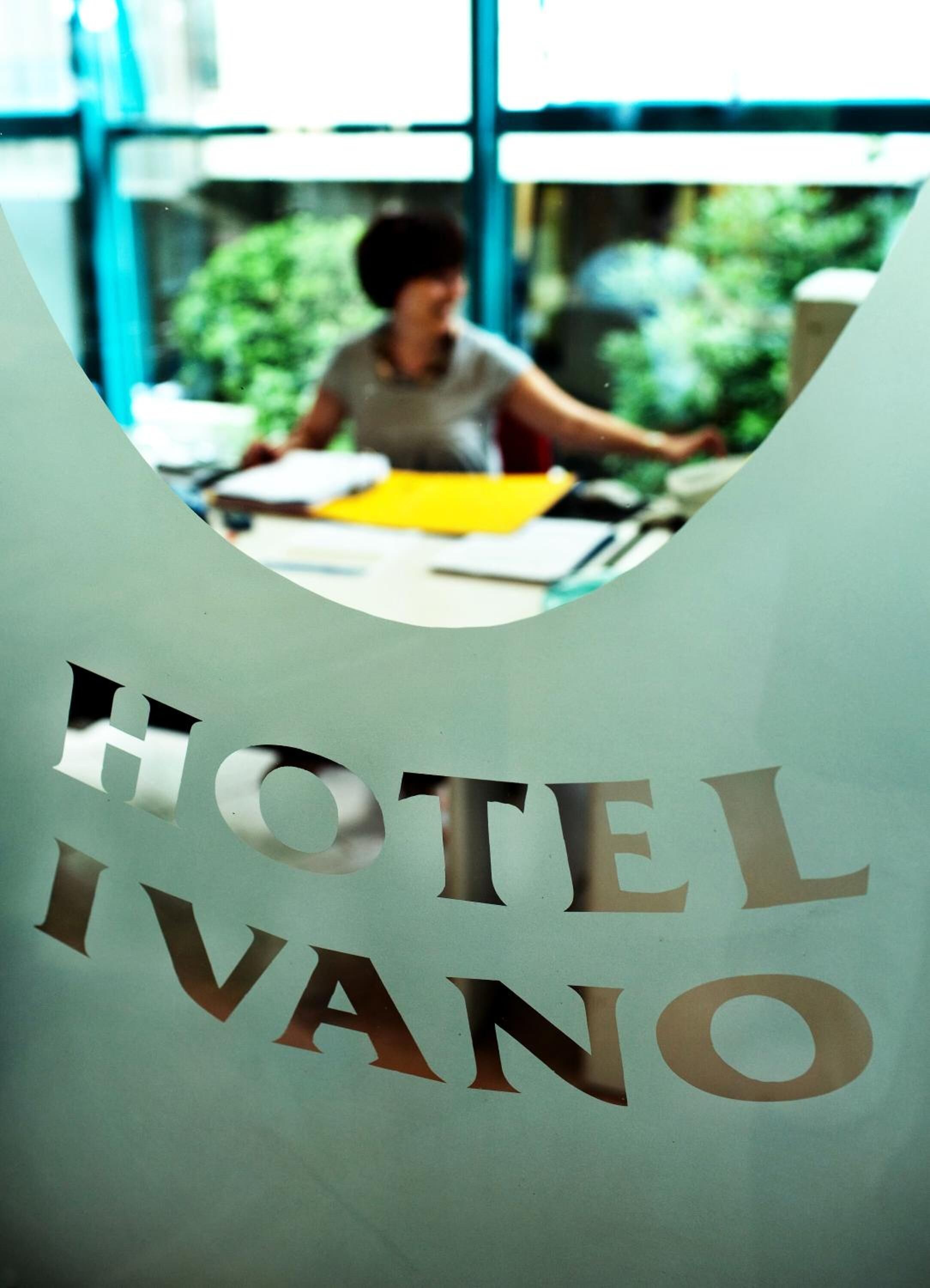 Vista a través de una ventana del HOTEL IVANO, con una persona trabajando en un escritorio.